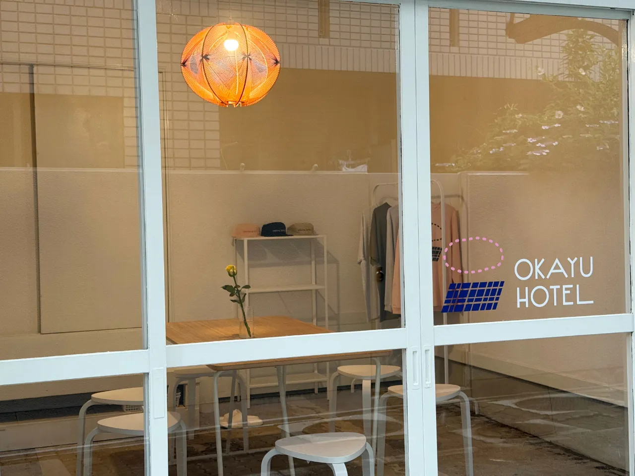 OKAYU HOTELの外観。ガラス戸にロゴが描かれ、店内には木のテーブルとオレンジ色の照明
